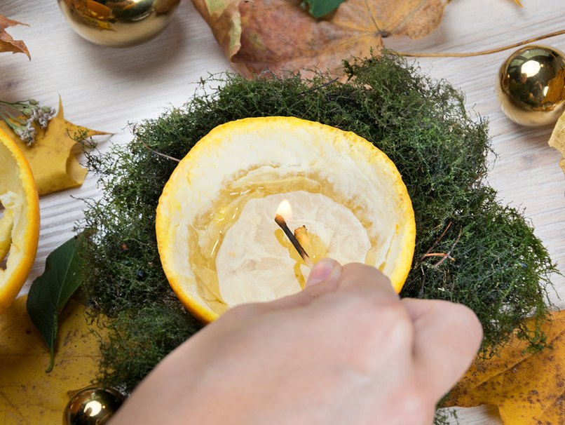 Orangenkerze mit Streichholz haltender Hand 